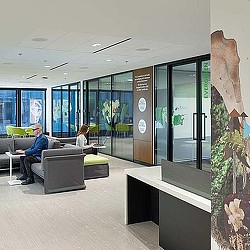 A man and a woman sitting on a couch in a room with glass walls and a sign.