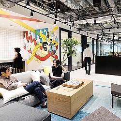 A group of people sitting on a couch in a room with a large screen and a person standing.