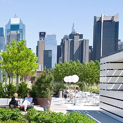A group of people sitting at tables in a courtyard with tall buildings in the background.