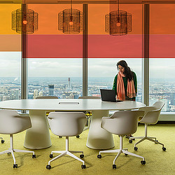 A person standing behind a table with a laptop and chairs in front of a window.