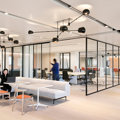 A room with a glass wall and a couple of people sitting at tables.