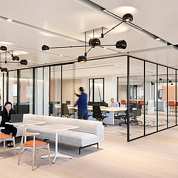 A room with a glass wall and a couple of people sitting at tables.