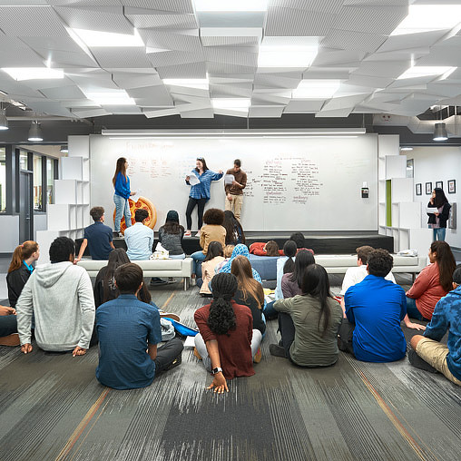 A group of people sitting in a room looking at a person standing on a stage.