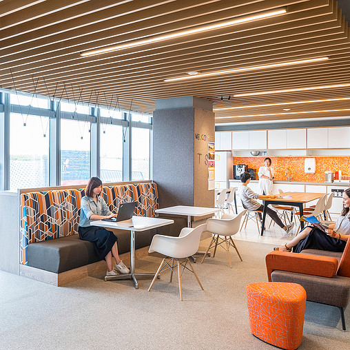 A group of people sitting in a room with orange chairs and tables.