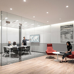 A group of people sitting in a room with a person standing in front of a glass wall.