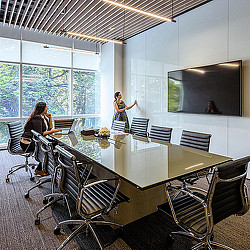 A person standing in front of a table with chairs and a screen.