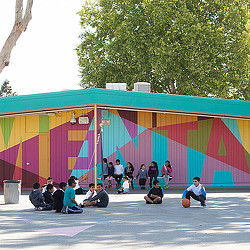 A group of people sitting on the ground in front of a colorful wall.