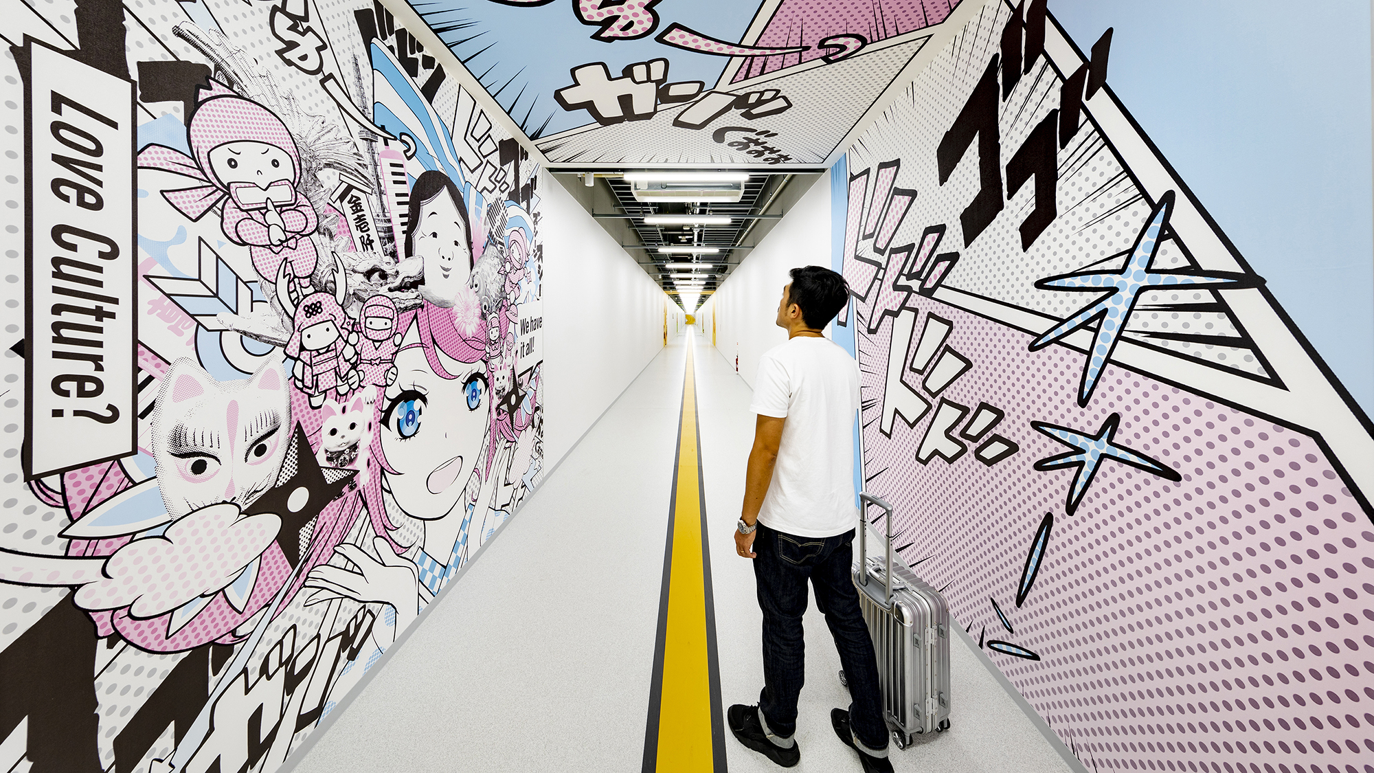 A passenger walks down a hallway with branded graphics inside an airport.