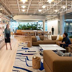 A woman standing in a room with a man sitting on a couch.