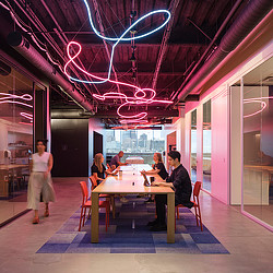 A group of people sitting at a table in a room with a large screen.