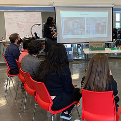A group of people sitting in a classroom looking at a screen.