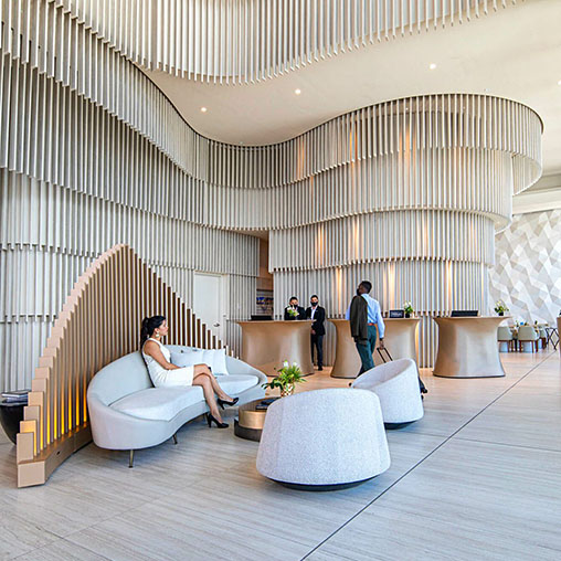 A person lying on a couch in a room with people walking around.