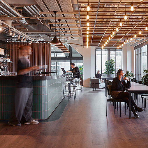 A person standing in a room with people sitting at tables and chairs.