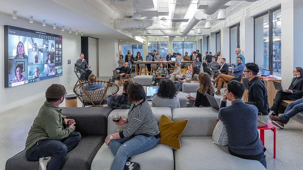 A group of people sitting in a room with a large screen.