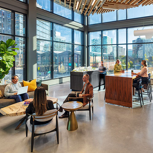 A group of people sitting in a room with windows and a table.