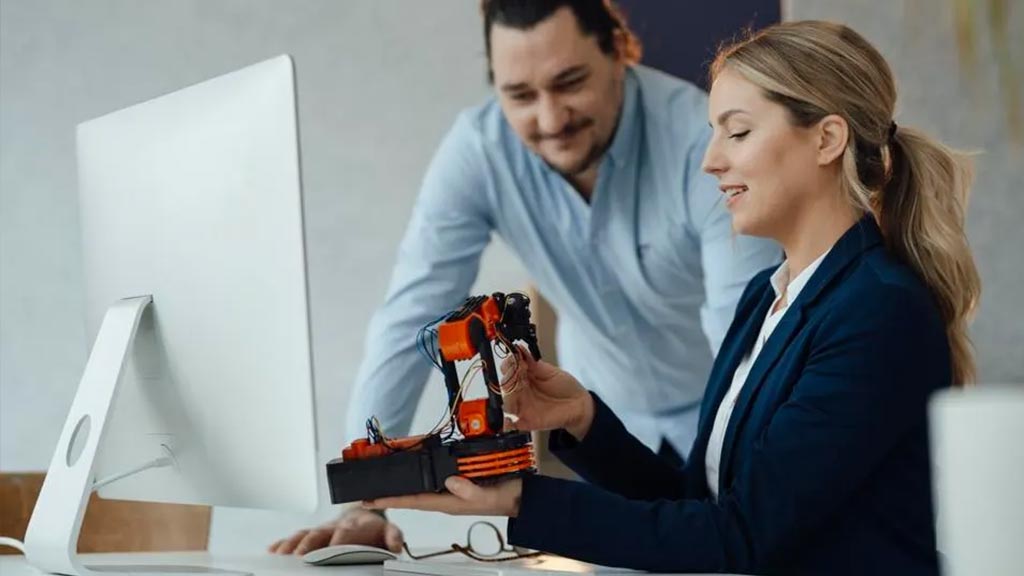 2 coworkers looking at robotic prototype at work. Credit: Getty