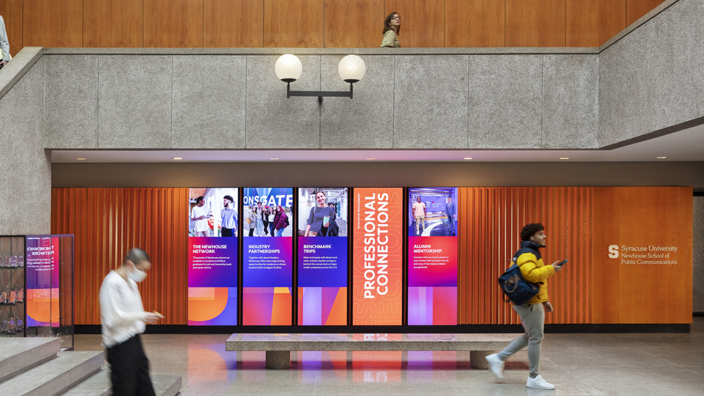 2 students walking by Syracuse University Newhouse School of Communications digital displays