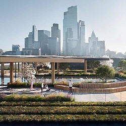 A group of people standing on a bridge over a river with a city in the background.