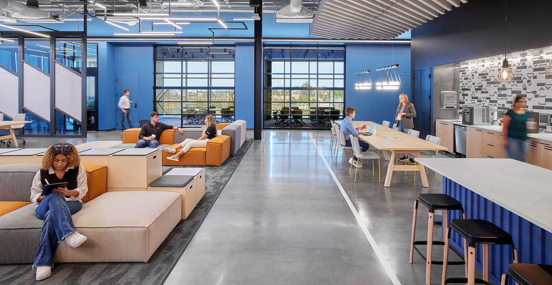 A group of people sitting in a room with windows and a table.