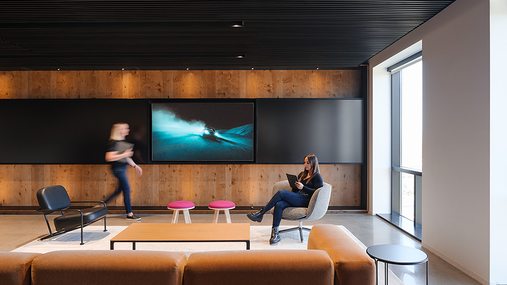 A person standing in front of a screen in a room with chairs.
