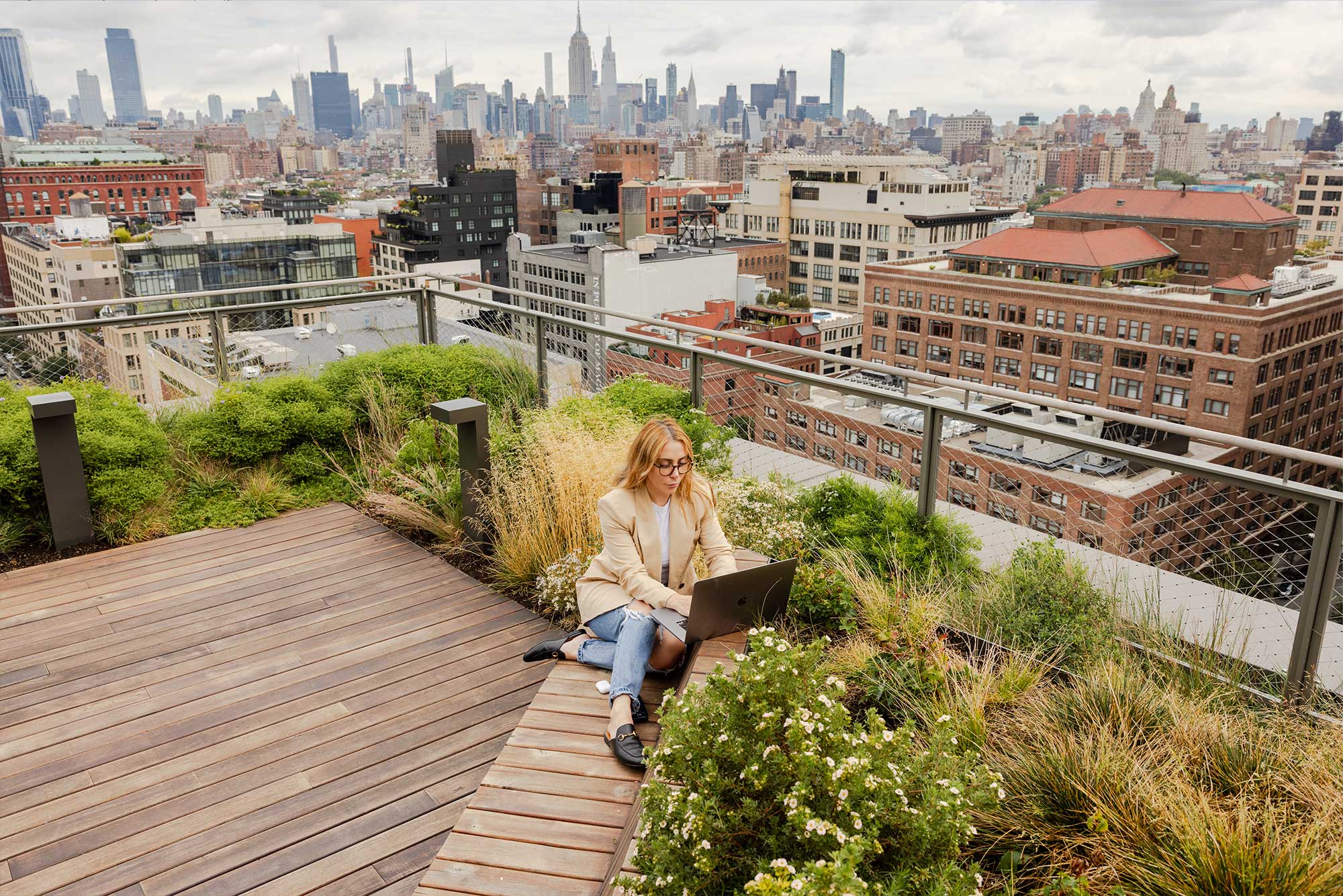 A woman working on her laptop on the High Line with views of New York