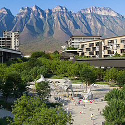 A large courtyard with buildings and trees with mountains in the background.