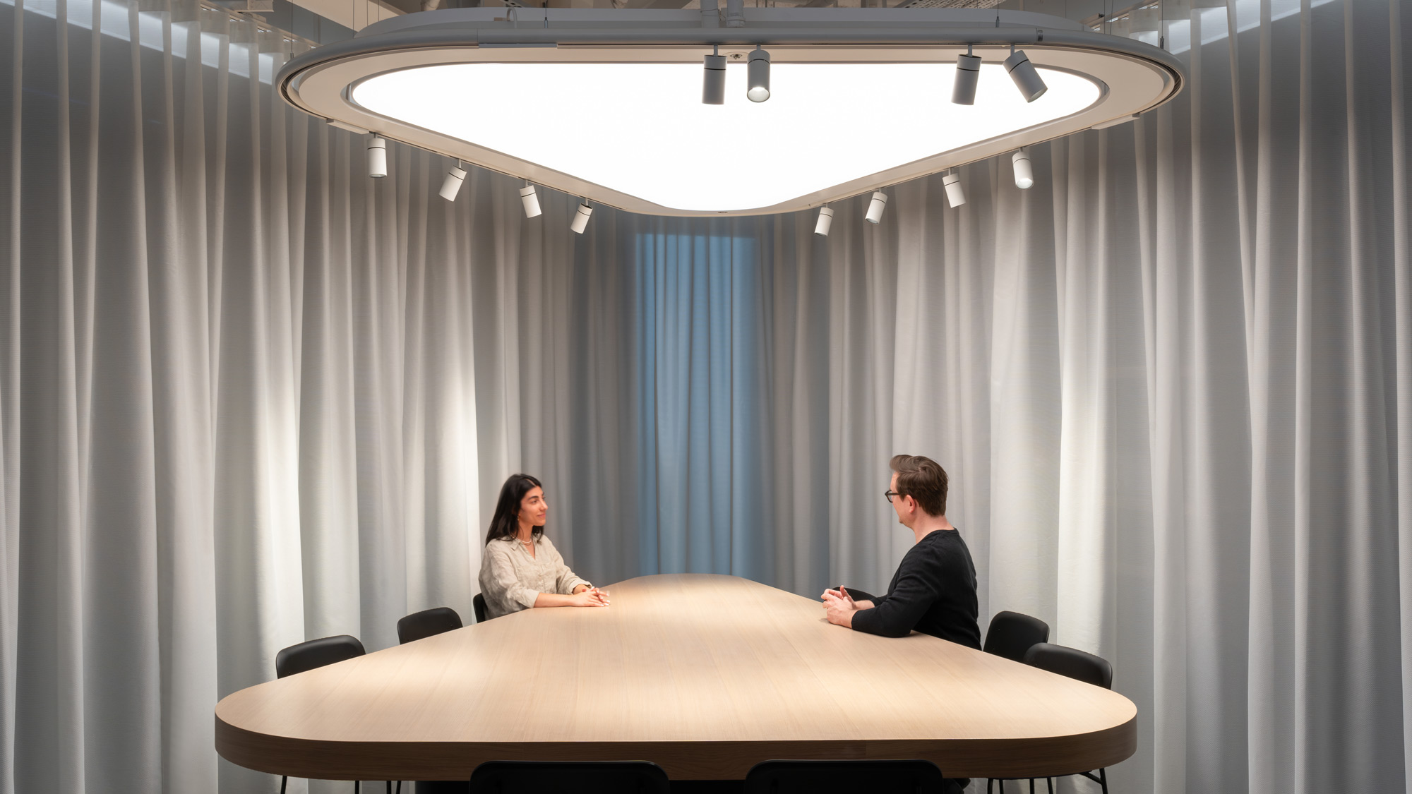 A man and a woman sitting at a table with a white table and chairs with a white curtain.