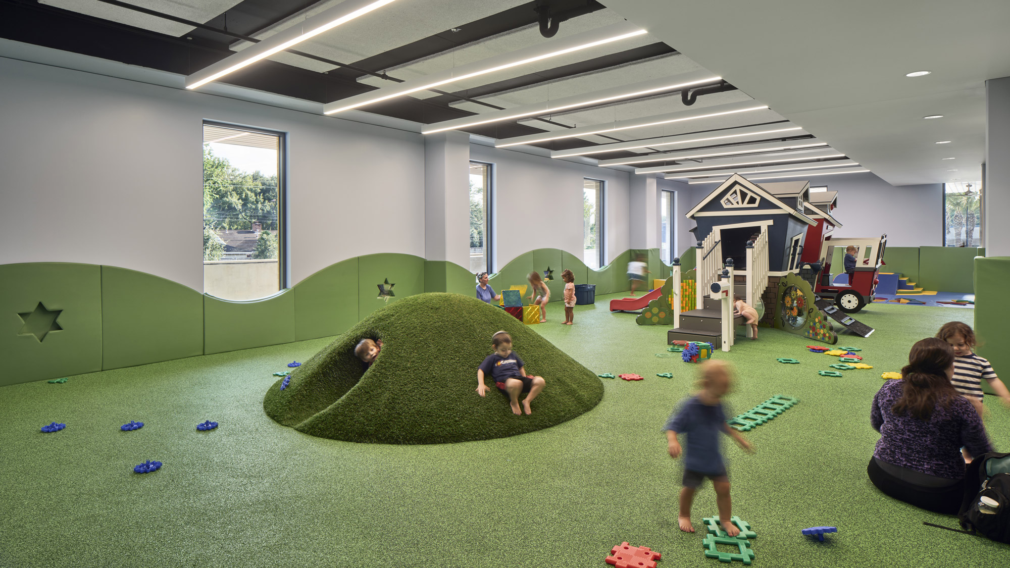 A group of people playing on a green trampoline in a room.