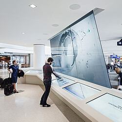 Airport traveler interacting with SFO T3 Boarding Area E digital screens
