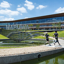 A couple of people running on a path by a pool and a building.