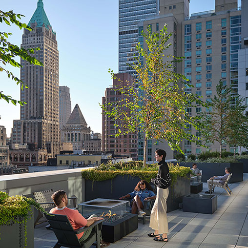 A group of people sitting on a bench in a park with tall buildings.
