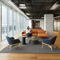 A person sitting on a couch in an office lounge room with a table and chairs.