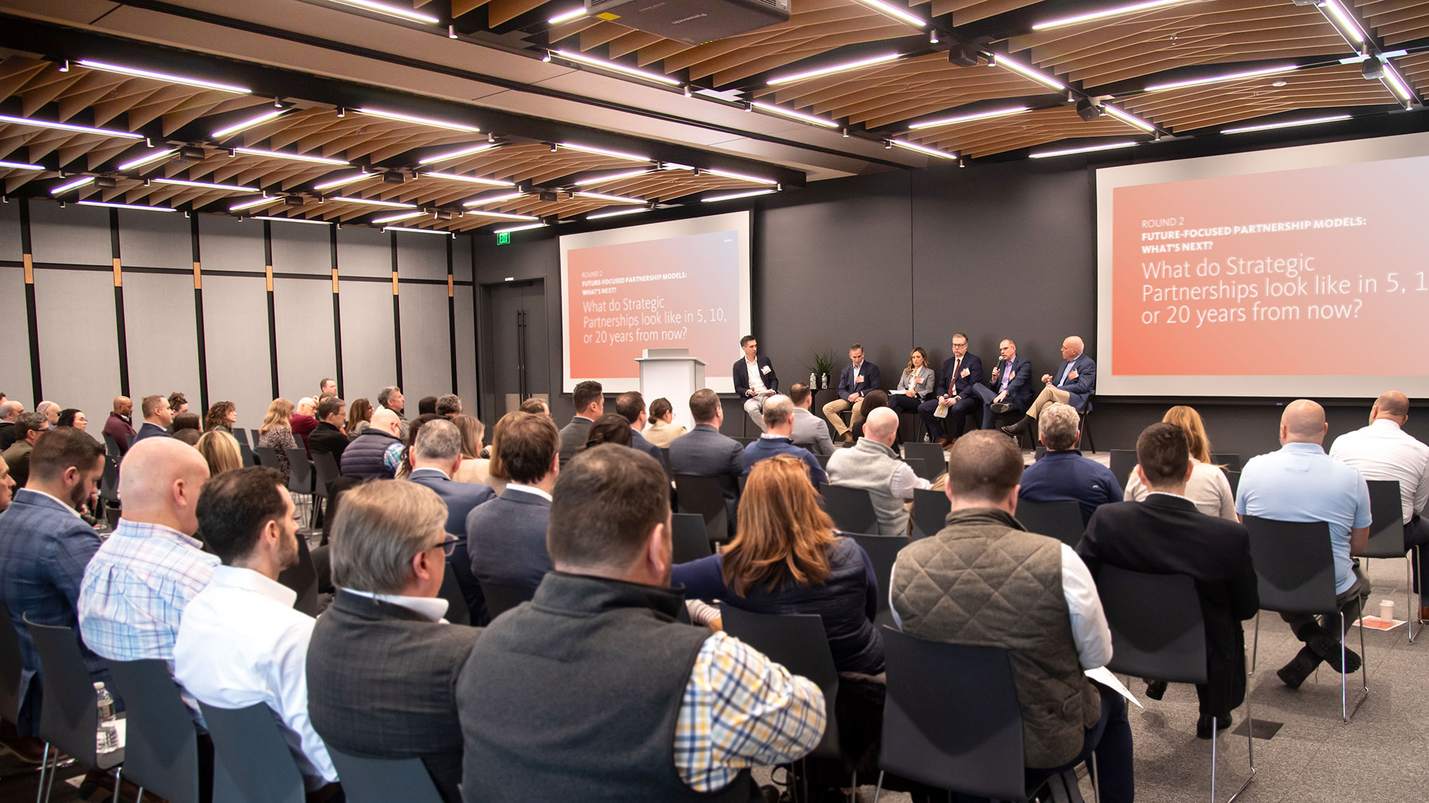 A group of people sitting in a room with a screen and a projection screen.