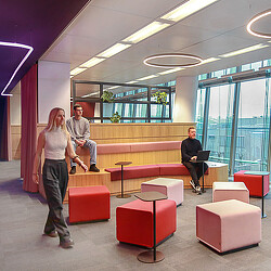 A woman standing in front of a man sitting on a red couch.