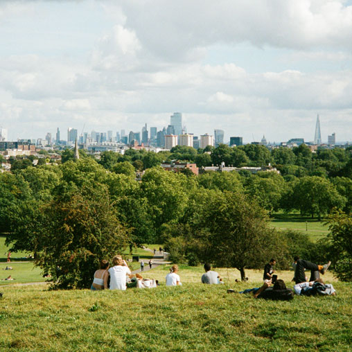 A group of people sitting on a grassy hill overlooking a city.