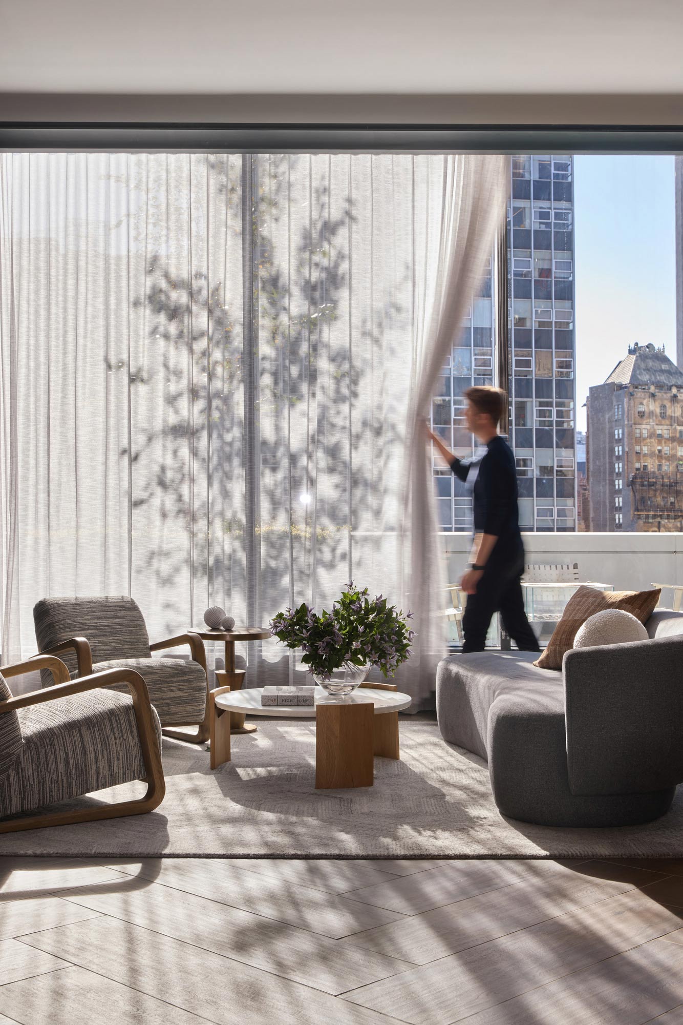 A person standing in a room with a window and a table with chairs.