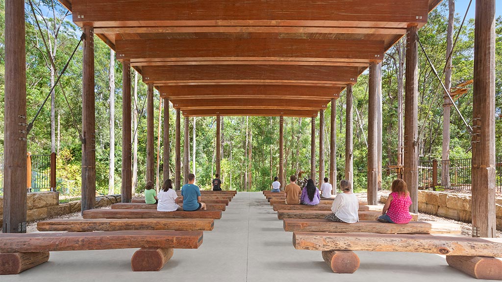 A group of people sitting on a bench under a covered area in Guulabaa.