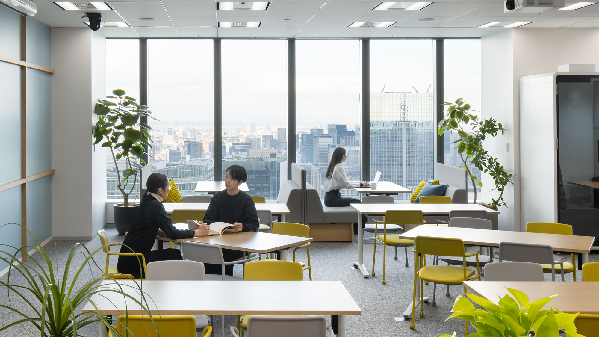 A group of people sitting at tables in a room with large windows.