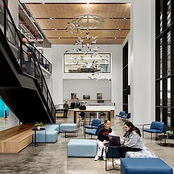 A group of people sitting in a room with blue chairs and a chandelier.
