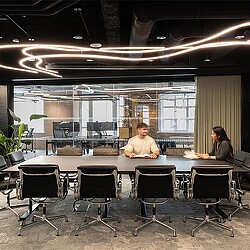 A man and woman sitting at a table in a room with chairs.